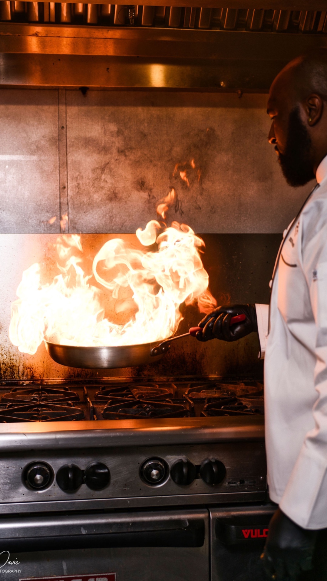 Chef Gilfert Hunt flambéing a pan over a professional range